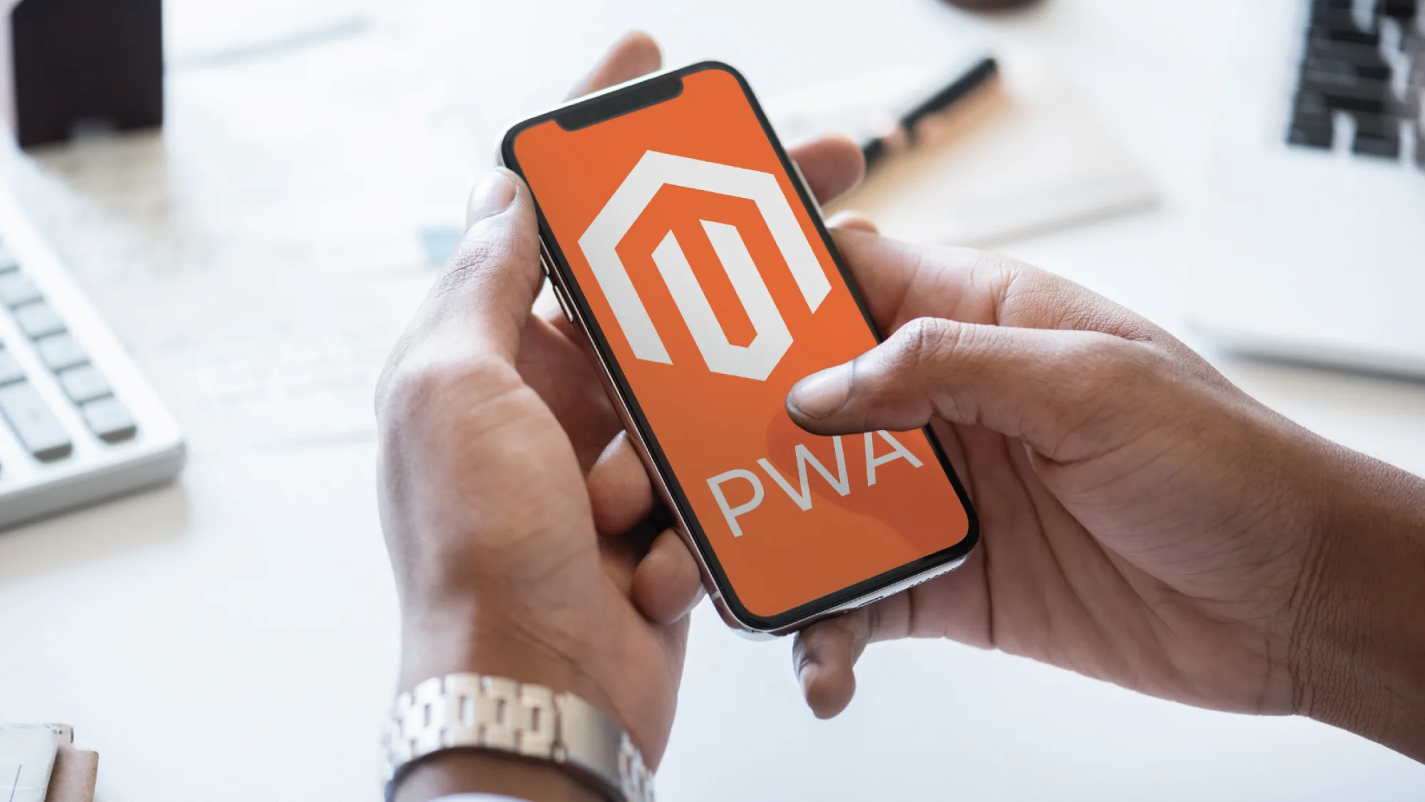A person holding a mobile phone with big Magento logo and PWA text written bellow.