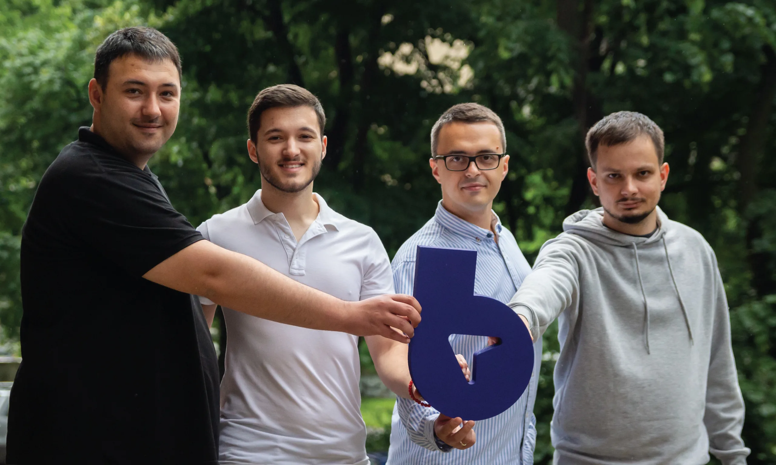 A team of four young mean holding a carboard logo in the park.